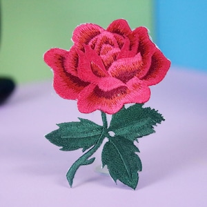 May include: A red embroidered rose with green leaves. The rose is a single bloom with a stem and leaves.