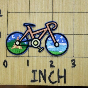May include: A pink bicycle with a blue and green tyre design. The front tyre has a night sky design with a crescent moon and stars. The back tyre has a daytime sky design with clouds and grass.