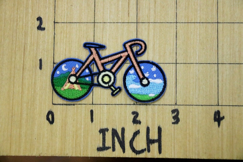 May include: A pink bicycle with a blue and green tyre design. The front tyre has a night sky design with a crescent moon and stars. The back tyre has a daytime sky design with clouds and grass.