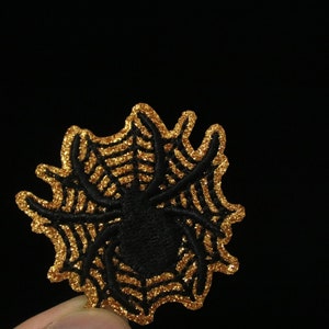 May include: A black spider embroidered on a gold glitter spiderweb.