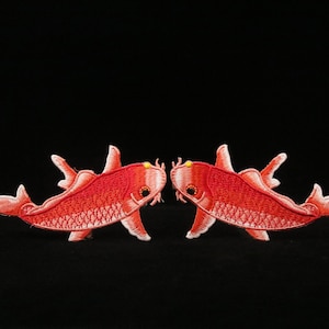 May include: Two red embroidered koi fish facing each other. The fish are detailed with white scales and have a yellow spot on their bodies.