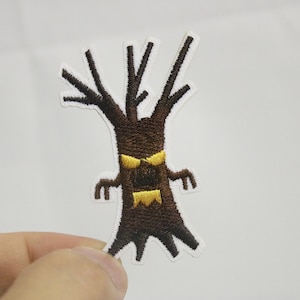 Può includere: Toppa ricamata da stirare di un albero marrone con un viso giallo arrabbiato. L'albero ha un'espressione minacciosa con due occhi gialli e una bocca gialla.