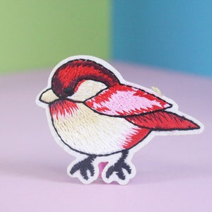 May include: Embroidered iron-on patch of a red and white bird with a pink breast. The bird is facing the right side of the image.