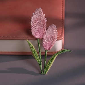 以下が含まれることがあります： 緑の葉が付いた刺繍入りのピンクの花のパッチ。 花柄のデザインは、ピンクの革張りのノートに配置されています。 パッチは詳細なステッチとテクスチャード加工の外観を備えており、衣類やアクセサリーに追加するのに最適です。