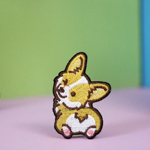 Puede incluir: Parche bordado de un perro corgi marrón y amarillo con marcas blancas. El corgi está mirando hacia la izquierda y tiene la lengua fuera.