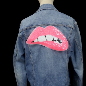 May include: A blue denim jacket with a pink sequined lips patch on the back.