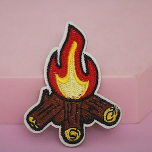 May include: Embroidered iron-on patch featuring a campfire with red and yellow flames and brown logs.