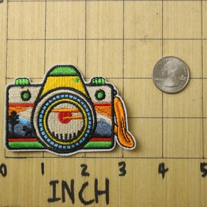 Puede incluir: Un parche bordado de colores para planchar que representa una c&aacute;mara vintage con una escena de puesta de sol en el visor. El parche mide aproximadamente 5 cm de ancho y 4 cm de alto.