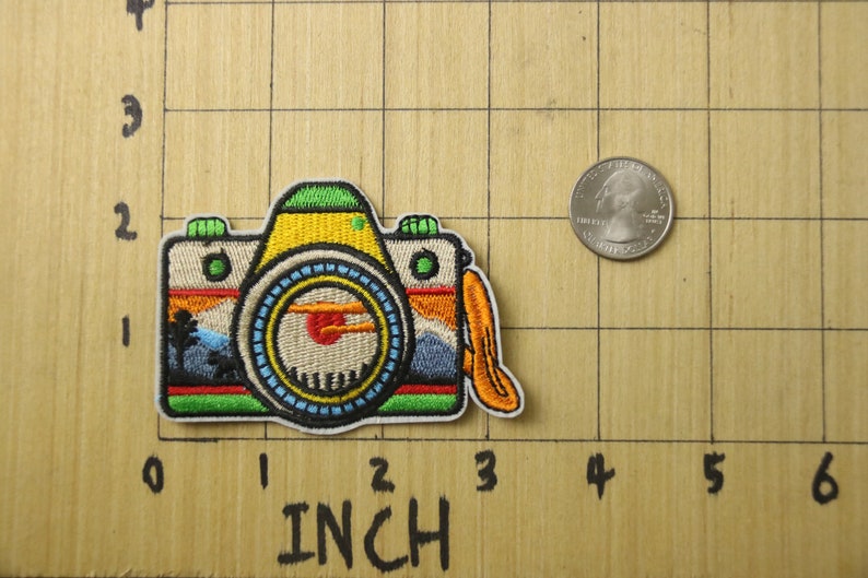 Puede incluir: Un parche bordado de colores para planchar que representa una c&aacute;mara vintage con una escena de puesta de sol en el visor. El parche mide aproximadamente 5 cm de ancho y 4 cm de alto.