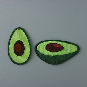 May include: Two green avocado-shaped embroidered patches with brown seeds. The patches are on a light gray background.