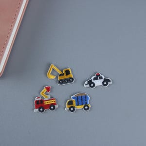 May include: Four embroidered iron-on patches featuring different vehicles: a yellow excavator, a red fire truck, a blue dump truck, and a white police car.