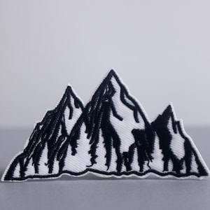May include: Embroidered mountain patch featuring a black and white design. The patch depicts a stylized mountain range with detailed black stitching on a white background. Ideal for jackets, bags, or other fabric items.