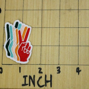Pu&ograve; includere: Toppa ricamata colorata a forma di simbolo della pace, con una mano rossa con dettagli bianchi e un bordo bianco. La toppa &egrave; stratificata con colori verde, turchese, pesca e arancione. La toppa misura circa 5 cm di altezza.