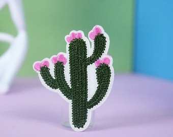 Könnte beinhalten: Ein grüner Kaktus mit rosa Blüten, gestickt auf einem weißen Stoffstück.