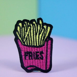 May include: A pink and black embroidered patch with a cartoon image of a container of french fries. The container is labeled "FRIES".