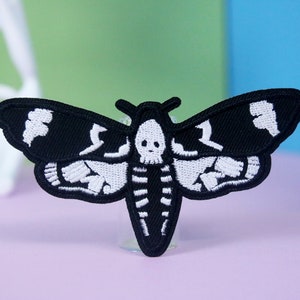 May include: Black and white embroidered iron-on patch of a moth with a skull design.