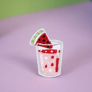 May include: White embroidered patch of a glass with pink and red watermelon juice and a slice of watermelon on top.