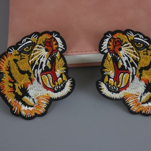 May include: Two embroidered iron-on patches featuring a roaring tiger head with yellow, orange, red, white, and black thread.