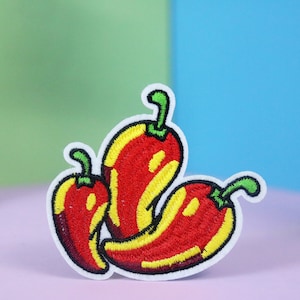 Könnte beinhalten: Drei gestickte Chilischoten in Rot, Gelb und Grün. Die Chilischoten sind in einer Gruppe angeordnet, wobei die größte Chilischote in der Mitte liegt.