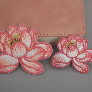 Könnte beinhalten: Zwei rosa gestickte Lotusblüten-Patches. Der größere Patch ist etwa 10 cm breit und der kleinere Patch etwa 5 cm breit.