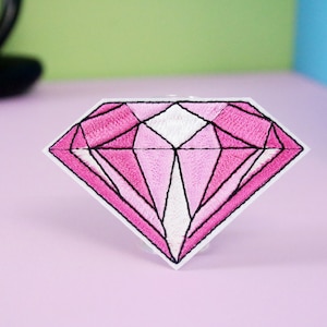 May include: Pink diamond shaped embroidered patch with black outline.