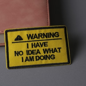 Può includere: Un cartello di avvertimento giallo con testo nero che dice "ATTENZIONE NON HO IDEA DI COSA STO FACENDO".