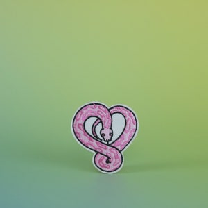 Op de afbeelding: Roze geborduurde patch van een slang die in de vorm van een hart is opgerold.