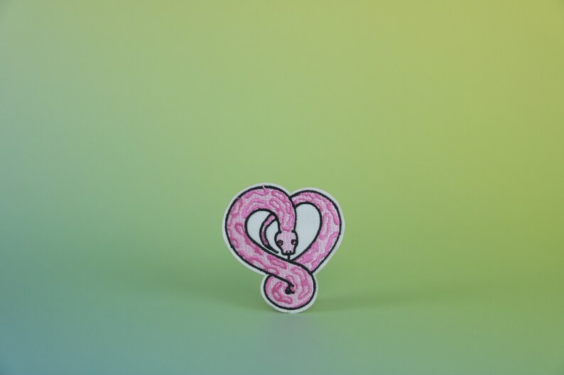 Op de afbeelding: Roze geborduurde patch van een slang die in de vorm van een hart is opgerold.