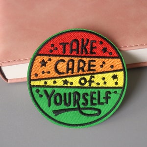 Könnte beinhalten: Ein runder, bunter gestickter Aufnäher mit dem Text "TAKE CARE OF YOURSELF" in schwarzen Buchstaben. Der Aufnäher hat eine rot-orange-gelb-grüne Farbgebung.