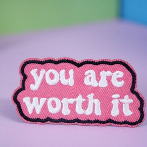 May include: Pink fabric patch with black stitching in the shape of a speech bubble. The text "you are worth it" is embroidered in white.