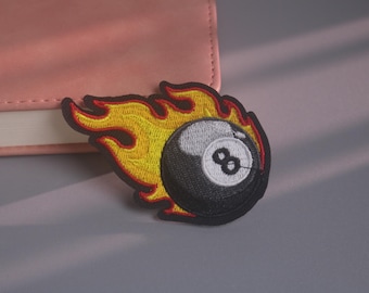 May include: An embroidered patch featuring a black eight ball with a white circular centre and the number eight in black, surrounded by stylised yellow and orange flames with a thick black border outline, creating a vibrant and detailed design.