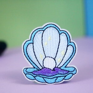 May include: Embroidered patch featuring a light blue seashell with a pearl and purple accents. The seashell design has a white border and is set against a colorful background. This patch is suitable for clothing or accessories.