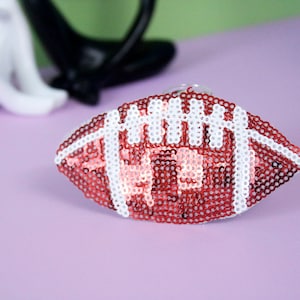 May include: A red and white football made of sequins. The football is a decorative item and is not meant for playing.