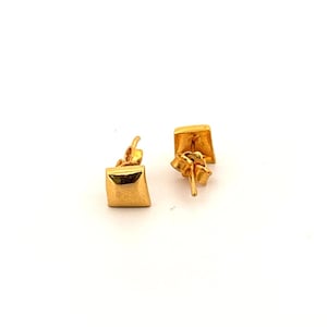 May include: A pair of gold stud earrings featuring a square, pyramid-shaped design. The earrings have a polished, reflective surface and include standard post-style backs for secure attachment, showcasing a simple geometric form.
