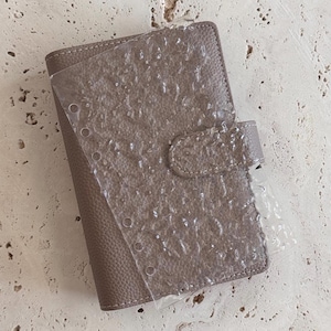 May include: A gray leather bound planner with a clear plastic sheet on top. The plastic sheet has holes for a binder.