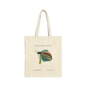 Op de afbeelding: Een beige tote bag met een kleurrijke illustratie van een kever met de tekst "A Study of Creatures Big and Small" en "Crystalwing Beetle" gedrukt op de voorkant.