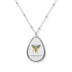 May include: Silver-toned necklace with an oval pendant featuring a Luminescent Lacewing illustration. The pendant showcases a colorful insect design with blue wings and a yellow body, with text that reads "Luminescent Lacewing".