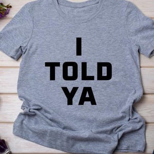 May include: A gray t-shirt with the text "I TOLD YA" printed in black.