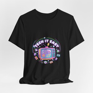 May include: Black t-shirt featuring a retro television graphic with the text "TECH IT EASY" in a circular design. The design includes a lightning bolt, a floppy disk, and other tech-related icons in a colorful, pastel palette.
