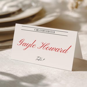 May include: A white folded place card featuring the text Oakley&Co. at the top, followed by the heading CARLA'S DINNER CLUB between two horizontal lines. The name Gayle Howard is printed in red script, with the text Table 4 below in black.