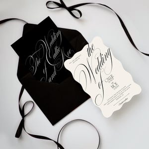 K&ouml;nnte beinhalten: Ein schwarzer Umschlag mit einer schwarzen Karte mit wei&szlig;er Kalligrafie, die The Wedding of Callie and Moe liest, neben einer cremefarbenen, gewellten Hochzeitseinladung mit schwarzem Text und einem schwarzen Band, das um das Set gebunden ist.
