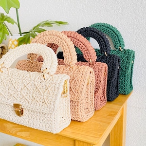 May include: Five crocheted handbags in different colors, including white, beige, pink, green, and black. The handbags have a unique woven design and gold hardware.