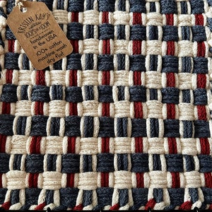 May include: A red, white, and blue woven pot holder with a tag that reads "KRISTIN KAYS LOOPSON LOOM handwoven in the USA 100% cotton machine wash dry flat".