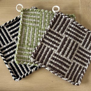 May include: Three woven pot holders with different patterns. One is black and white, one is green and white, and one is brown and white.