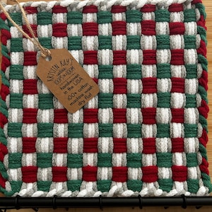 May include: A red, white, and green woven pot holder with a brown tag that reads "cellous LOOPS ON A LOOM handwoven in the USA KRISTIN KAY'S 100% cotton machine wash dry flat".