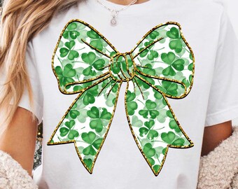 Peut inclure: T-shirt blanc avec un grand motif de nœud vert rempli de trèfles. Le nœud a une bordure dorée pailletée et un centre doré. Le t-shirt est de style décontracté, parfait pour la Saint-Patrick ou au quotidien.