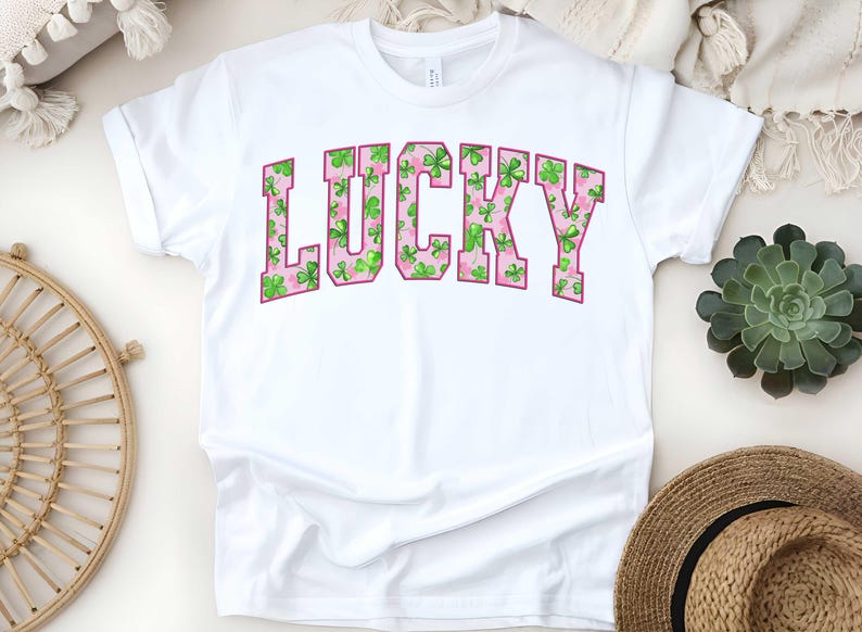 May include: White t-shirt with the word "LUCKY" printed in pink letters. The letters are filled with a pattern of green shamrocks.