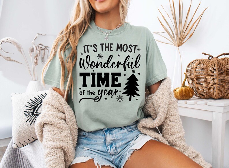 Pu&ograve; includere: Una maglietta verde chiaro con il testo "It's the most wonderful time of the year" in nero. Il testo &egrave; circondato da fiocchi di neve e stelle. Un piccolo albero di Natale &egrave; incluso anche nel design.