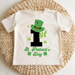 May include: White t-shirt with a green shamrock hat, a black number one, and the text "1st St. Patrick's Day".