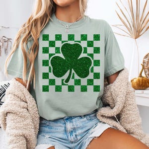 May include: A light green t-shirt with a green glitter shamrock on a green and white checkered background.